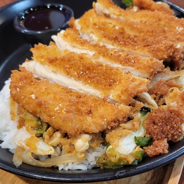 Crispy fried chicken katsu, sliced and served over white rice with a side of dark sauce.