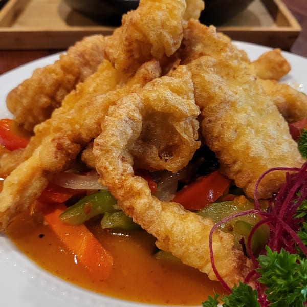 Crispy fried fish with sweet and sour sauce, bell peppers, onions, and carrots on a white plate.