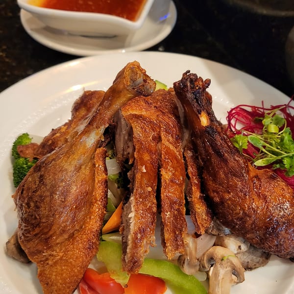 Crispy duck with vegetables and a side of sauce on a white plate at Nakama Sushi Thai.