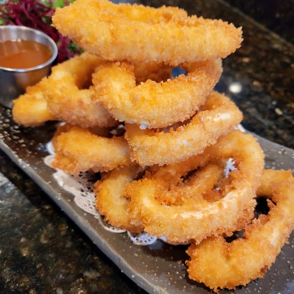 Crispy golden fried calamari rings stacked on a dark plate with a side of dipping sauce.
