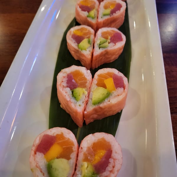 Heart-shaped sushi rolls with tuna, salmon, avocado, and mango on a white plate with a green leaf.