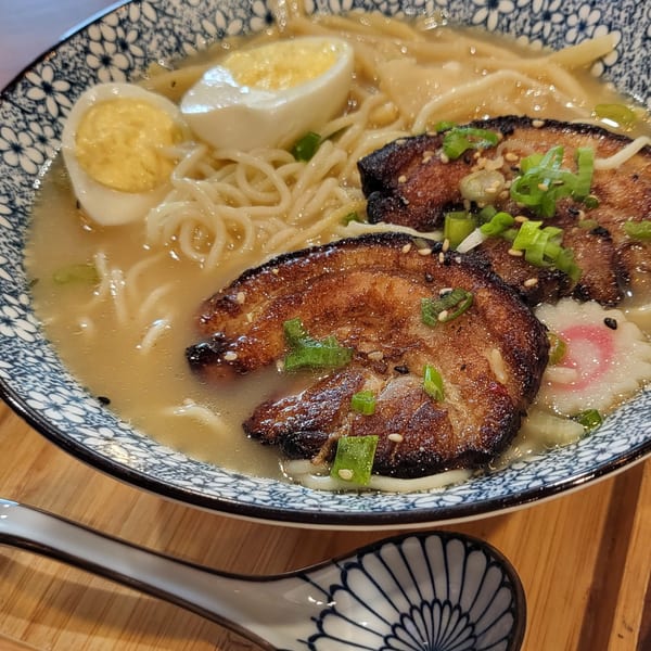 A bowl of Nakama Sushi Thai ramen with pork, egg, noodles, and green onions.