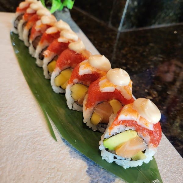 A row of Nakama Sushi Thai rolls with red topping, avocado, and mango, on a banana leaf.