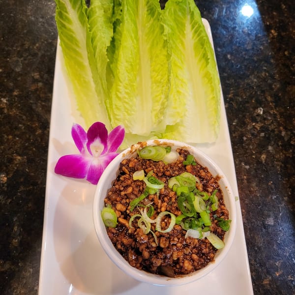 Thai lettuce wraps with minced chicken and green onions, served with fresh romaine lettuce and an orchid.