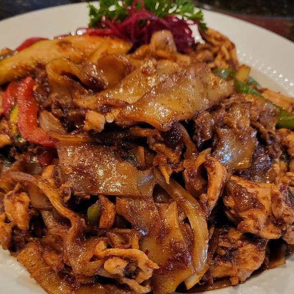 Close-up of a Thai dish with wide noodles, chicken, red peppers, and green vegetables.