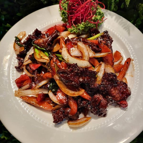 Thai beef stir-fry with onions, peppers, and scallions, garnished with red shredded vegetables.