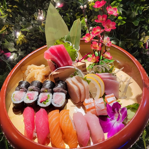 A large platter of Nakama Sushi Thai sushi and sashimi, garnished with pink flowers and green leaves.