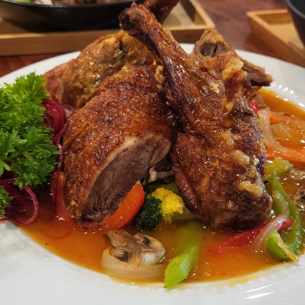 Crispy duck with vegetables and a rich sauce, garnished with parsley on a white plate.