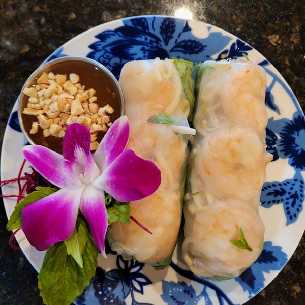Two fresh Thai spring rolls with shrimp, a peanut dipping sauce, and an orchid garnish.